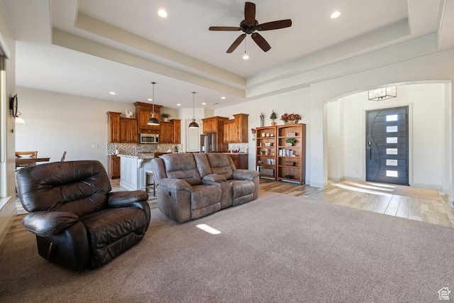living room with a tray ceiling, light hardwood / wood-style flooring, and ceiling fan