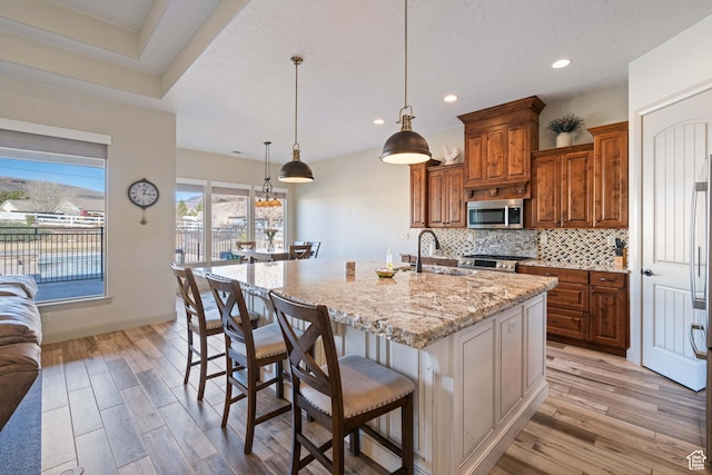 kitchen with sink, hanging light fixtures, a kitchen breakfast bar, tasteful backsplash, and a center island with sink