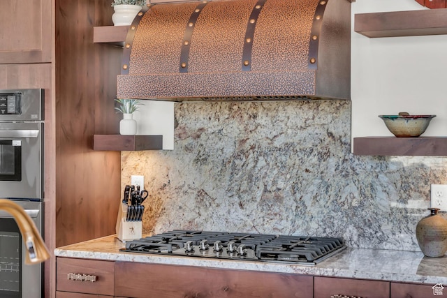 kitchen featuring appliances with stainless steel finishes, decorative backsplash, light stone counters, and ventilation hood
