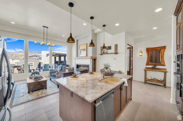 kitchen featuring light stone counters, an island with sink, stainless steel appliances, pendant lighting, and a sink