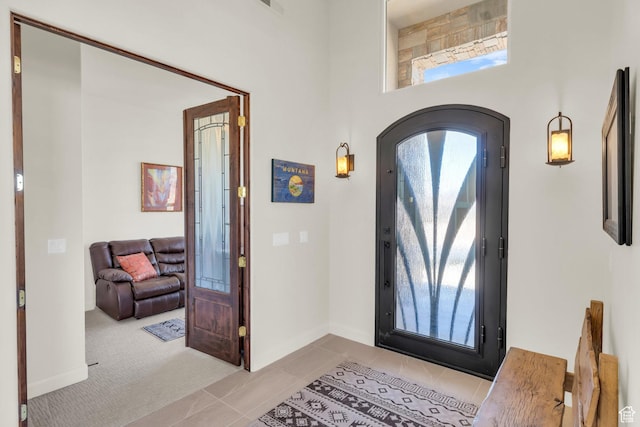 entryway featuring arched walkways, light tile patterned floors, a high ceiling, and baseboards