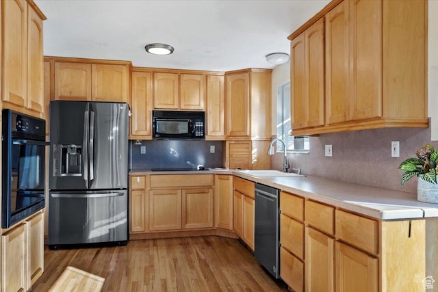 kitchen featuring tasteful backsplash, sink, light hardwood / wood-style flooring, and black appliances