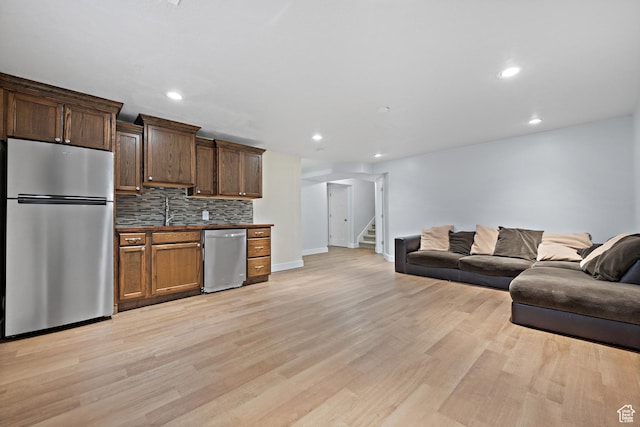 kitchen featuring stainless steel appliances, open floor plan, light wood-type flooring, baseboards, and decorative backsplash