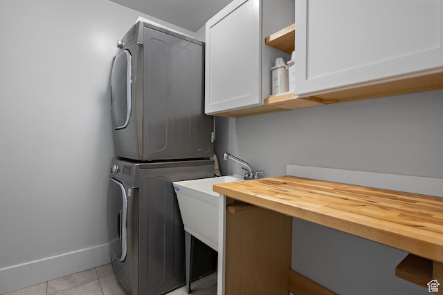 laundry room with light tile patterned floors, baseboards, stacked washing maching and dryer, and cabinet space
