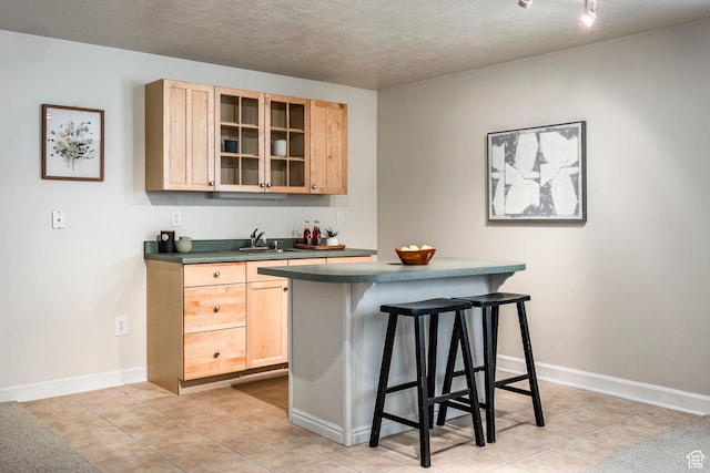 bar featuring light brown cabinetry, sink, a textured ceiling, and light tile patterned floors
