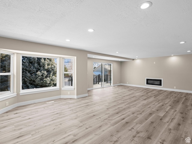 unfurnished living room with light hardwood / wood-style floors and a textured ceiling