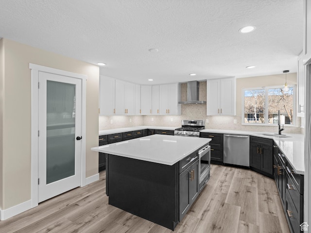 kitchen with a kitchen island, appliances with stainless steel finishes, pendant lighting, white cabinetry, and wall chimney range hood