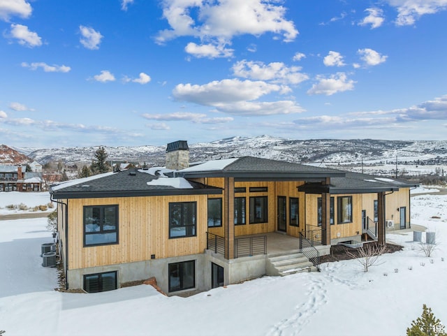 snow covered rear of property with a shingled roof, a chimney, and a mountain view