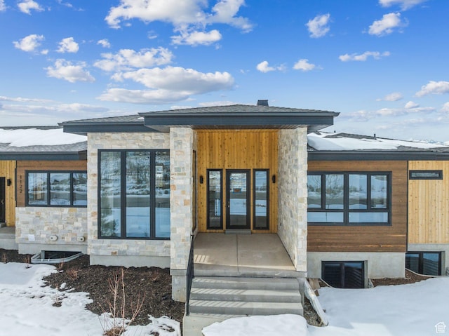 snow covered property entrance featuring stone siding and visible vents