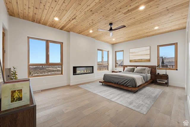 bedroom featuring recessed lighting, a glass covered fireplace, wood ceiling, and light wood-style floors