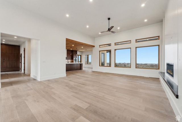 unfurnished living room with a healthy amount of sunlight, a glass covered fireplace, a towering ceiling, and light wood-style floors