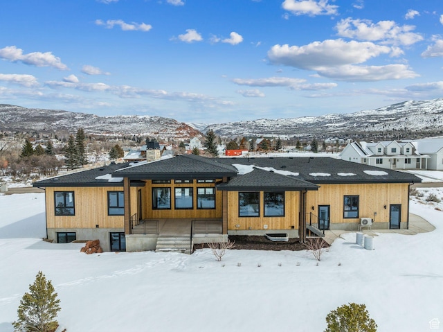 snow covered back of property featuring roof with shingles and a mountain view