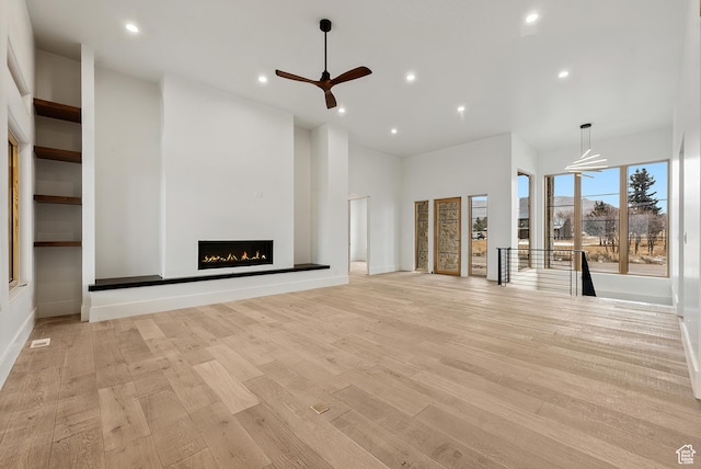 unfurnished living room featuring baseboards, ceiling fan, a lit fireplace, light wood-style floors, and recessed lighting
