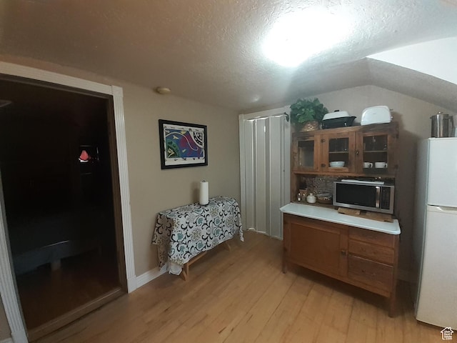 kitchen featuring stainless steel microwave, freestanding refrigerator, light wood-type flooring, glass insert cabinets, and a textured ceiling