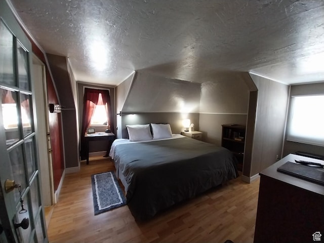 bedroom with light wood finished floors, baseboards, a textured ceiling, and multiple windows