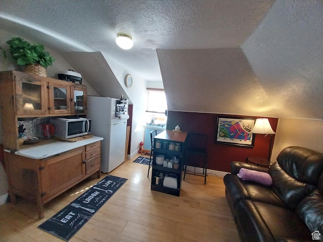 kitchen with stainless steel microwave, freestanding refrigerator, vaulted ceiling, and a textured ceiling