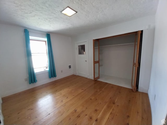 unfurnished bedroom featuring light wood finished floors, baseboards, a textured ceiling, and a closet