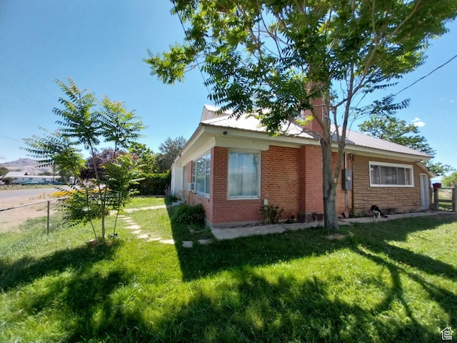 view of home's exterior with fence, a lawn, brick siding, and metal roof