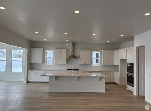 283 E Polaris Dr Unit 102, Saratoga Springs, UT 84045 - kitchen with double oven, wall chimney range hood, an island with sink, and white cabinets