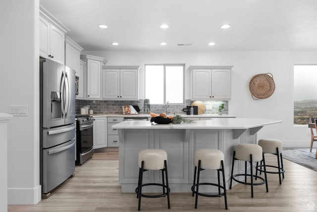 kitchen with a kitchen bar, backsplash, a kitchen island, light hardwood / wood-style floors, and stainless steel appliances