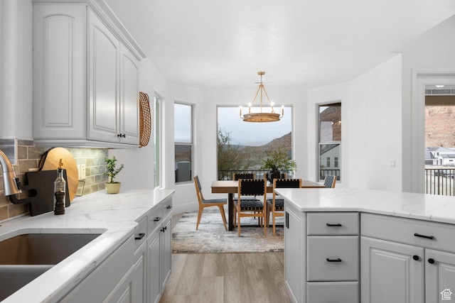 kitchen featuring light hardwood / wood-style flooring, decorative light fixtures, decorative backsplash, sink, and white cabinetry