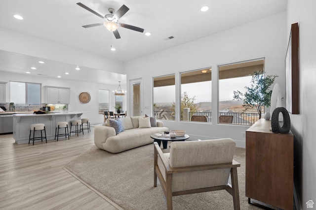 living room with sink, light hardwood / wood-style floors, and ceiling fan with notable chandelier