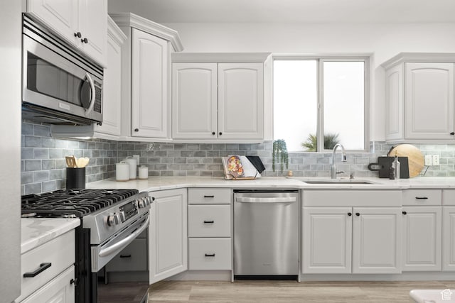 kitchen featuring appliances with stainless steel finishes, light stone counters, decorative backsplash, sink, and white cabinetry
