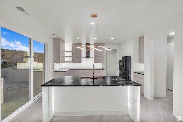 kitchen featuring sink, wall chimney range hood, high end black refrigerator, an island with sink, and decorative light fixtures