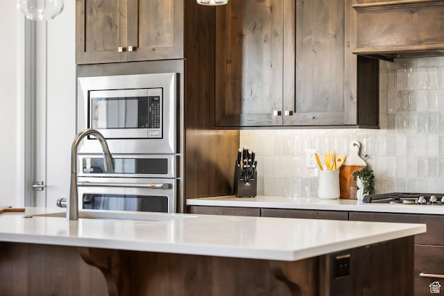 kitchen featuring premium range hood, sink, dark brown cabinets, appliances with stainless steel finishes, and backsplash