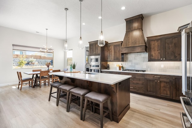 kitchen with pendant lighting, a kitchen island with sink, stainless steel appliances, decorative backsplash, and custom exhaust hood