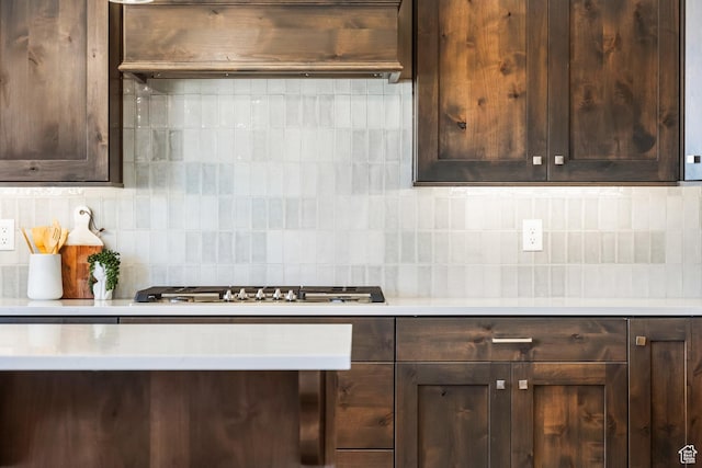 kitchen with dark brown cabinets, stainless steel gas cooktop, decorative backsplash, and exhaust hood
