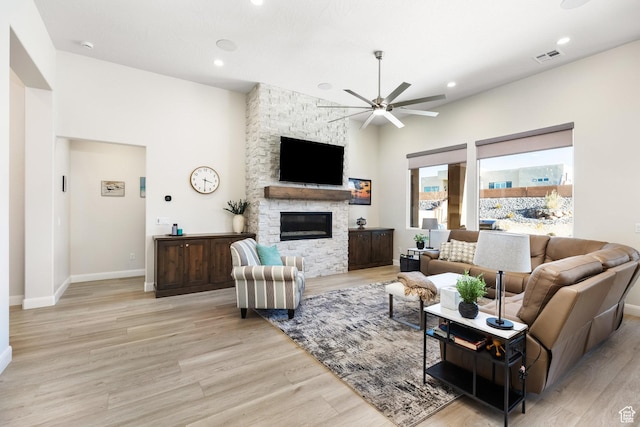 living room with a stone fireplace, light hardwood / wood-style floors, and ceiling fan