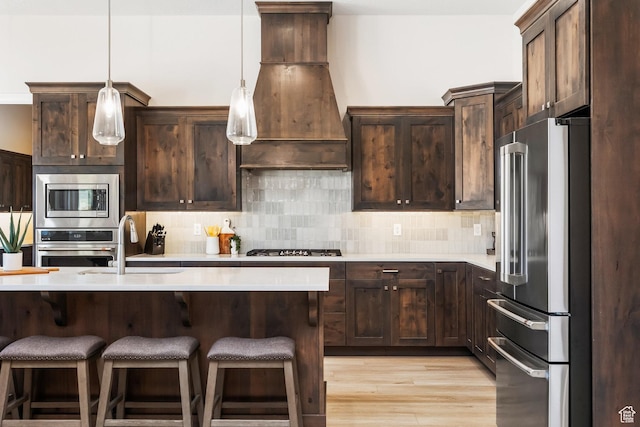 kitchen featuring premium range hood, dark brown cabinetry, hanging light fixtures, stainless steel appliances, and decorative backsplash
