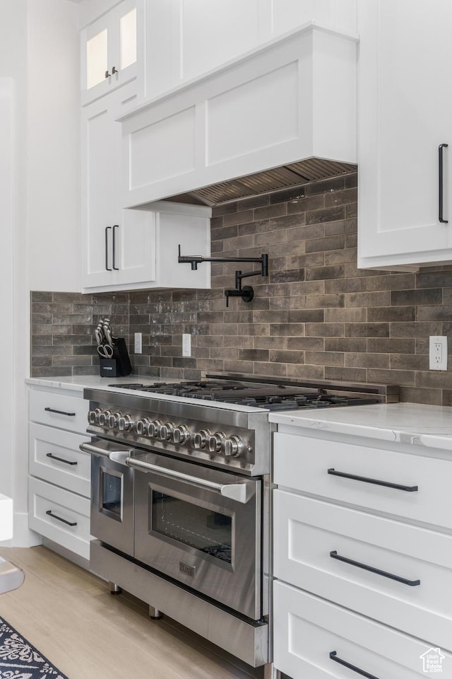 802 E Prairie Way, Washington, UT 84780 - kitchen with white cabinetry, range with two ovens, light stone countertops, custom range hood, and light wood-type flooring