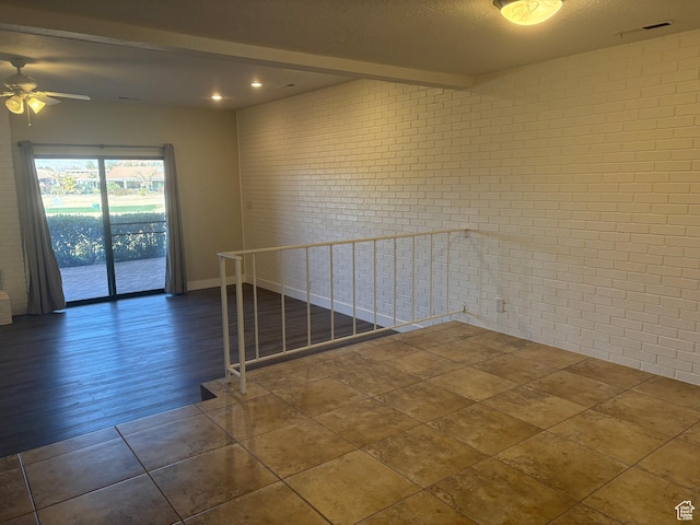 tiled empty room featuring beam ceiling, a textured ceiling, ceiling fan, and brick wall