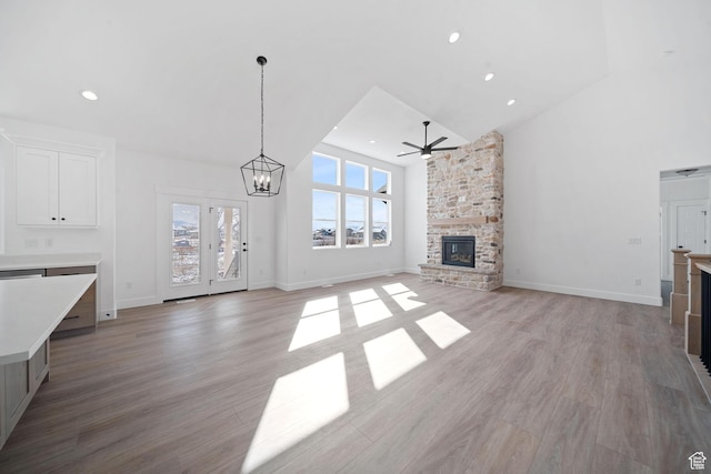 unfurnished living room with ceiling fan with notable chandelier, high vaulted ceiling, a fireplace, and light hardwood / wood-style floors