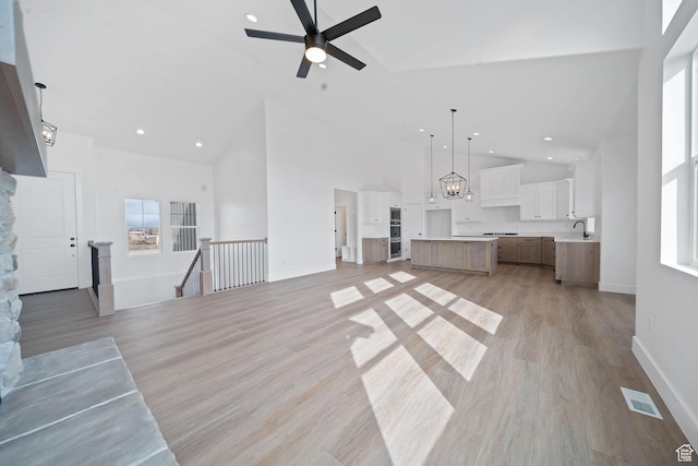unfurnished living room with light hardwood / wood-style flooring, sink, a wealth of natural light, and high vaulted ceiling