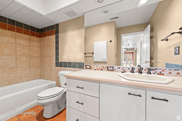 full bathroom with tile walls, tile patterned flooring, vanity, tiled shower / bath combo, and toilet