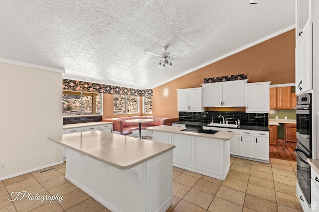 kitchen featuring sink, vaulted ceiling, a center island, and white cabinets