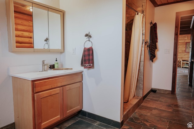 full bathroom with a shower with shower curtain, stone finish floor, vanity, and baseboards