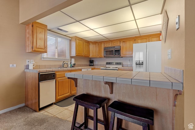kitchen with a sink, white refrigerator with ice dispenser, range with electric stovetop, stainless steel microwave, and tile countertops
