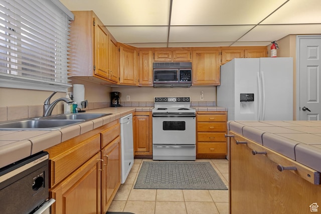 kitchen featuring light tile patterned flooring, a sink, tile countertops, white appliances, and a paneled ceiling