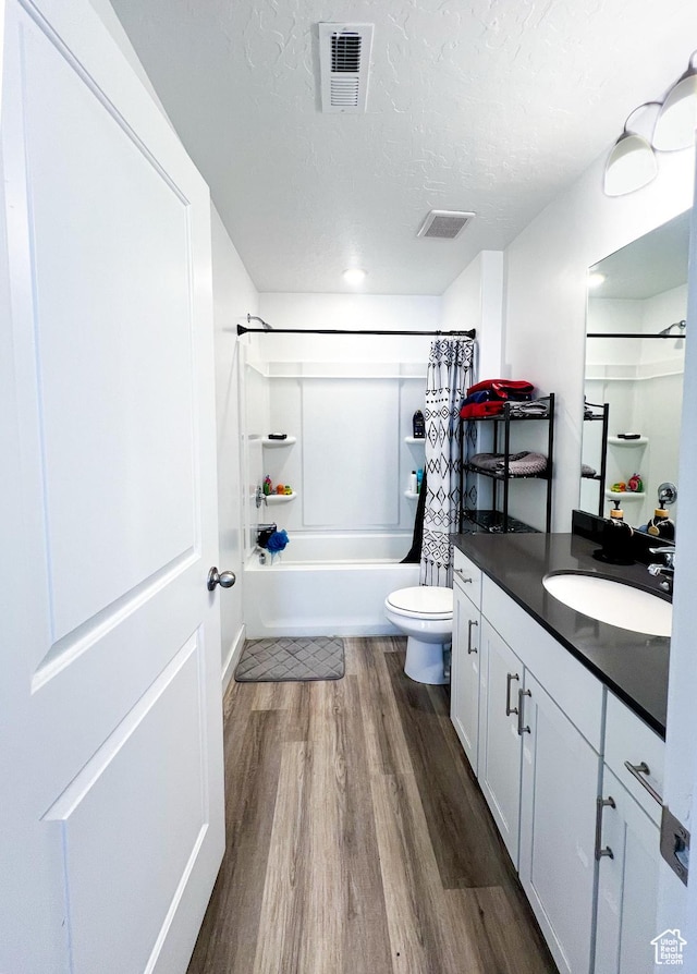full bathroom featuring hardwood / wood-style flooring, vanity, toilet, a textured ceiling, and shower / bath combo with shower curtain