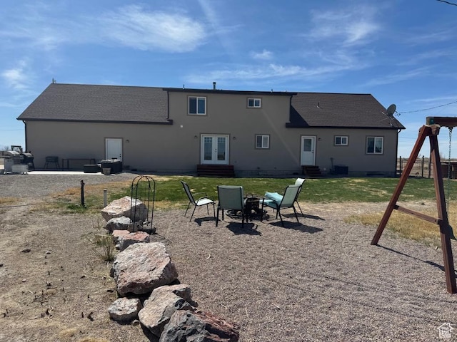 rear view of house with entry steps, central air condition unit, french doors, a lawn, and roof with shingles