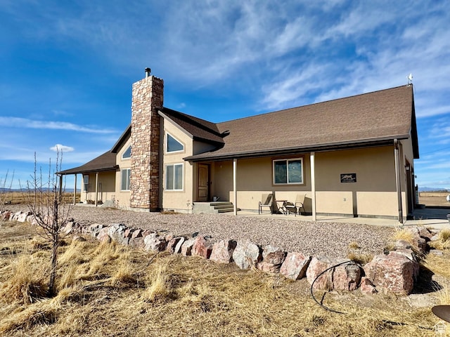 rear view of house featuring stucco siding, a chimney, and a shingled roof