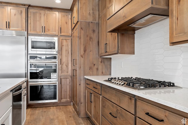 434 W 450 S Unit 815, Farmington, UT 84025 - kitchen featuring appliances with stainless steel finishes, custom exhaust hood, backsplash, light wood-style floors, and brown cabinets