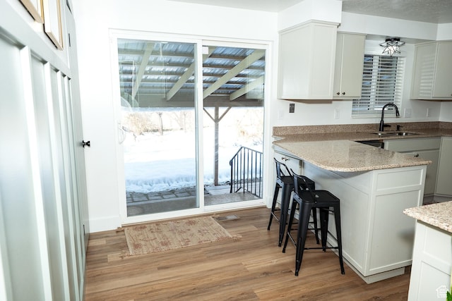 kitchen featuring light stone counters, a breakfast bar area, a peninsula, a sink, and light wood-type flooring