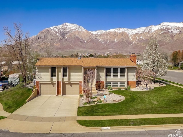 raised ranch featuring brick siding, a mountain view, a garage, driveway, and a front lawn