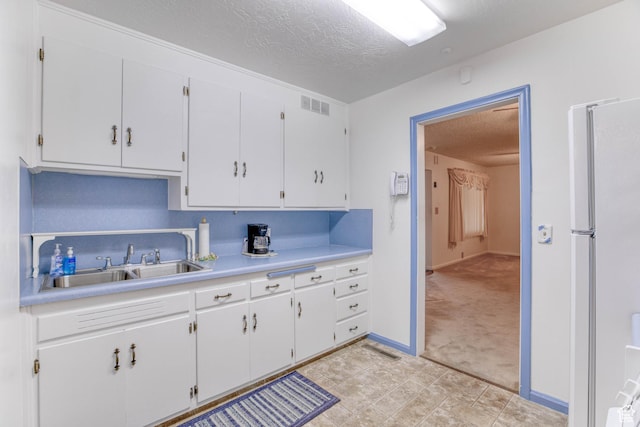 kitchen featuring white refrigerator, white cabinetry, sink, and a textured ceiling
