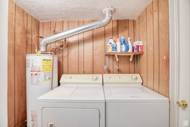 clothes washing area featuring a textured ceiling, wooden walls, water heater, and washing machine and clothes dryer